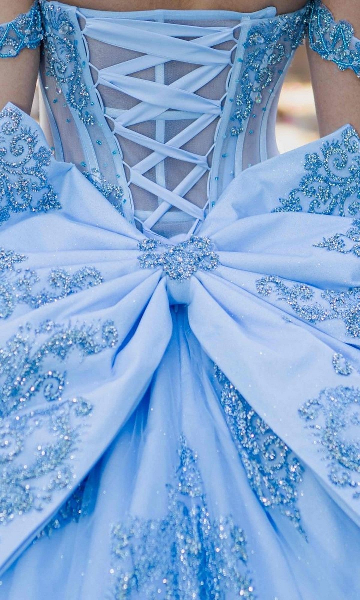 A close-up of the Quinceanera Dress 8190J by Cinderella Couture, a blue ball gown adorned with glittery embroidery, featuring a large bow and crisscrossed corset lacing on the back. This off-the-shoulder design evokes timeless elegance, perfect for special occasions.